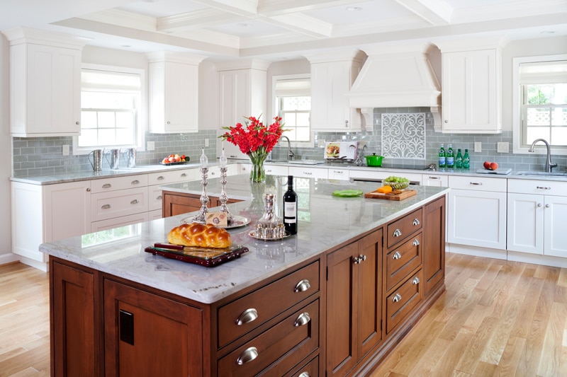 A large kitchen with white cabinets, gray backsplash and countertops, and wooden L-shaped island