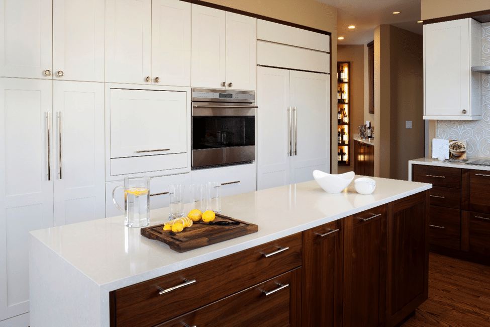 Remodeled kitchen with wood-grain island, white stone waterfall countertop, white cabinets, and wood floors.
