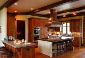A medium warm wood kitchen with 2 islands and a breakfast bar, recesses lighting, and wood beams on the ceiling
