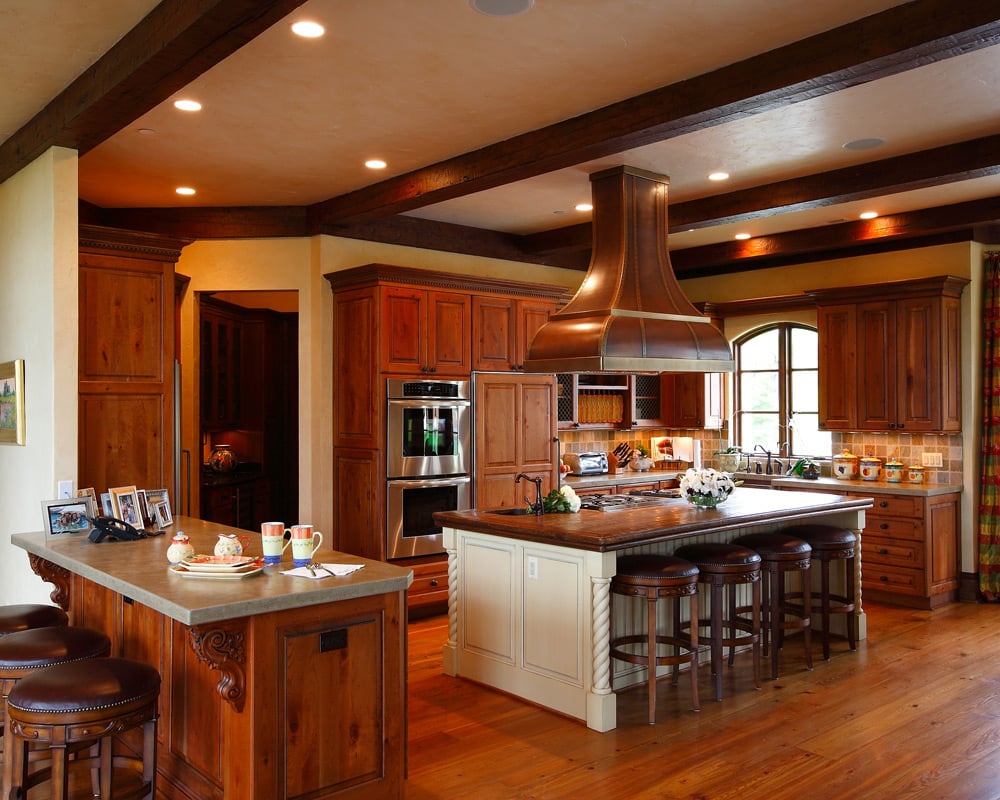 A medium warm wood kitchen with 2 islands and a breakfast bar, recesses lighting, and wood beams on the ceiling