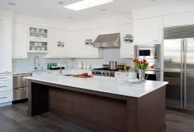 An all-white kitchen with a large L-shaped island made of a medium dark wood