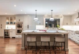 A grey and white kitchen with lots of built-in cabinetry and a large island with white marble countertop.