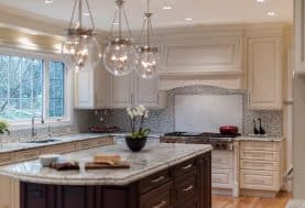 a beige and dark wood kitchen with a large center island and 3 glass light fixtures over it