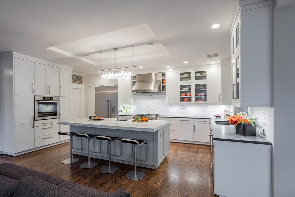 An all-white kitchen with silver appliances and recessed lighting