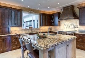 A kitchen with dark wood cabinetry, beige backsplash and grey marble center island