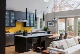 An open-concept living space with a minimalistic black kitchen with a yellow back splash.