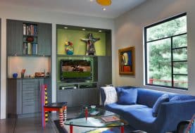 A colourful living room corner with a blue couch, glass coffee table and cool toned built-in shelving and media console